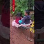 Pai leva filhos de carro de mão ao ponto de ônibus para irem à escola em dia de chuva