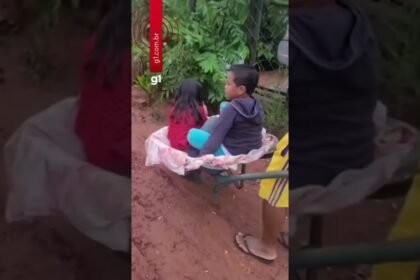 Pai leva filhos de carro de mão ao ponto de ônibus para irem à escola em dia de chuva