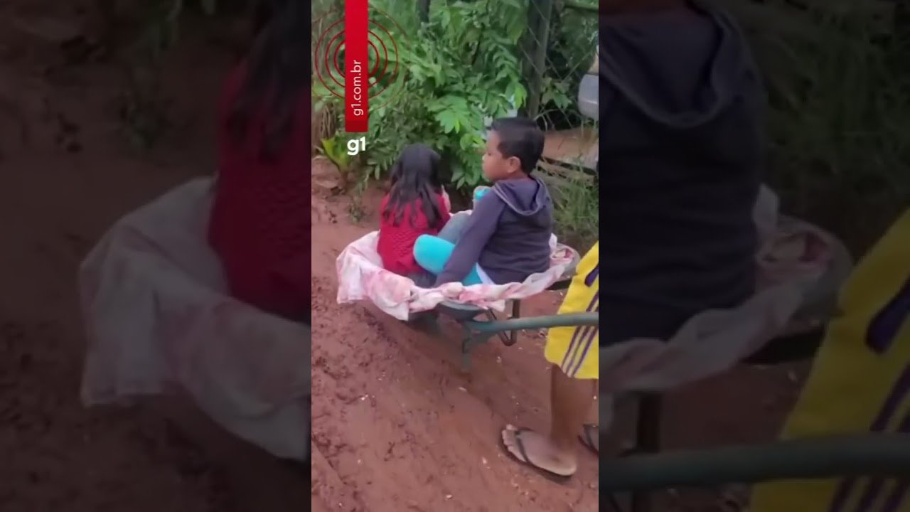 Pai leva filhos de carro de mão ao ponto de ônibus para irem à escola em dia de chuva